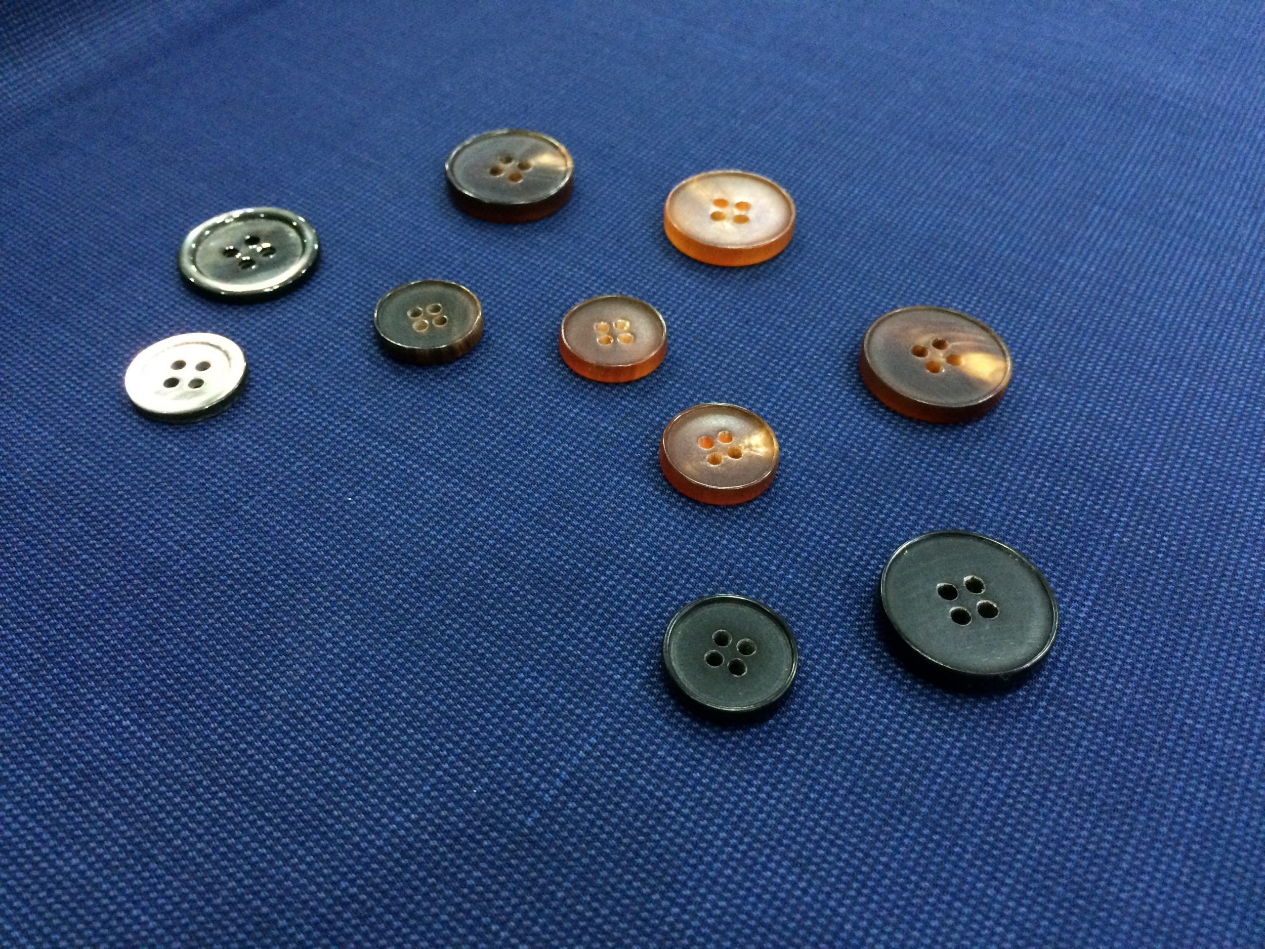A selection of four-hole buttons in different colours and sizes arranged on blue fabric.