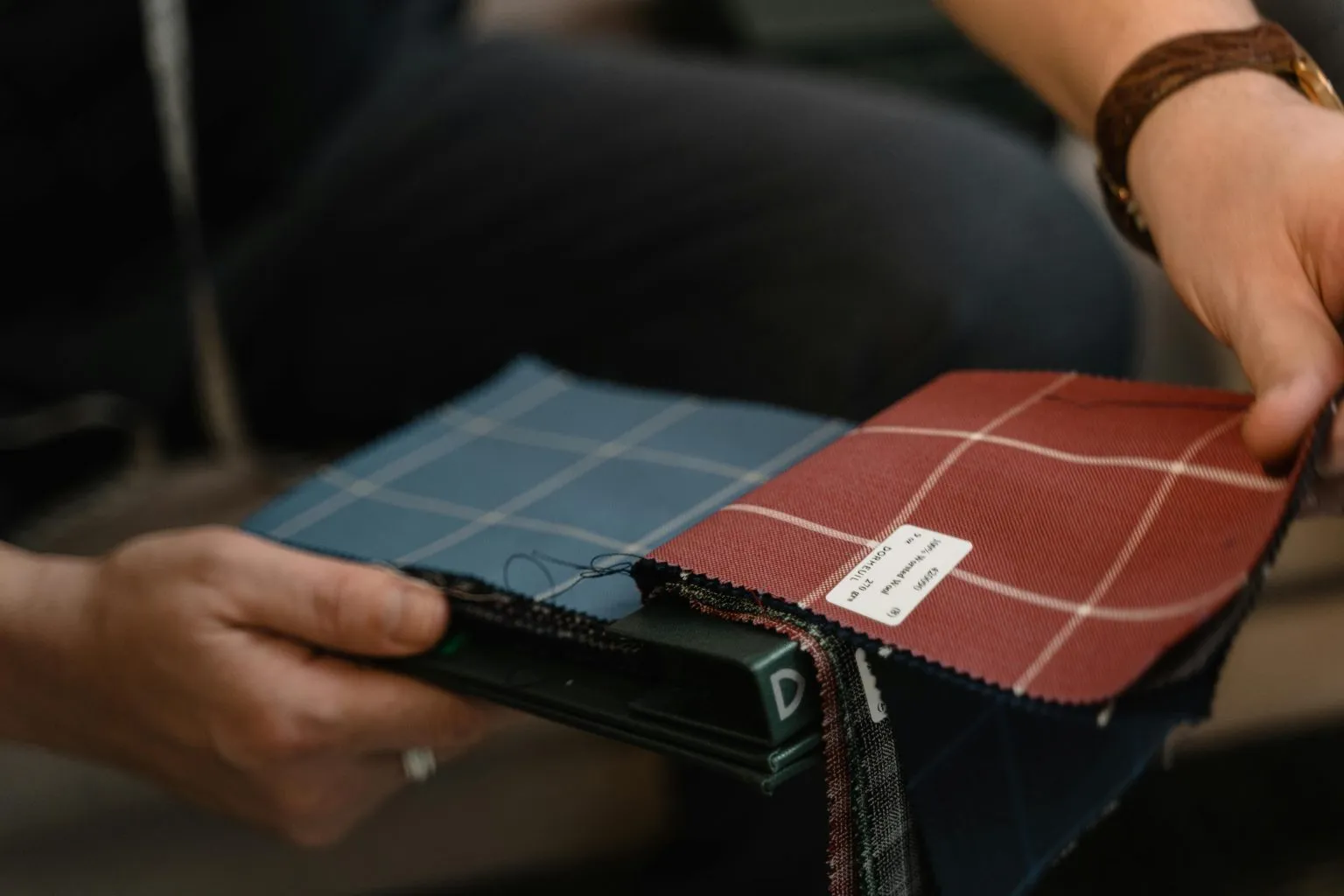 Hands holding blue and red checked suit fabric swatches.