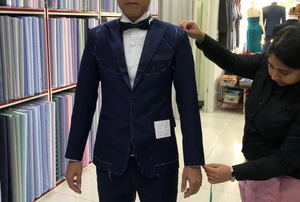 A fitter checking the shoulder and sleeve of a navy suit jacket with visible basting stitches.