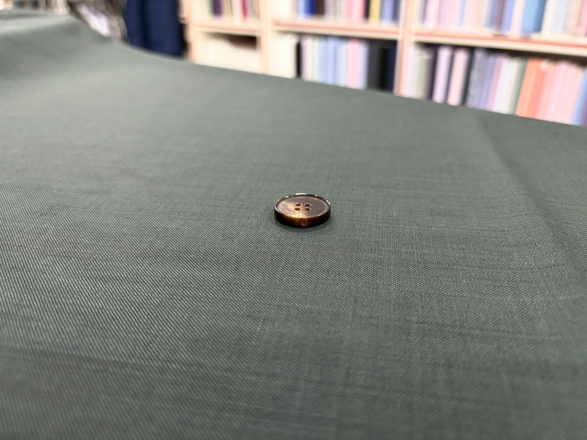 A dark brown four-hole button resting on textured forest green fabric.