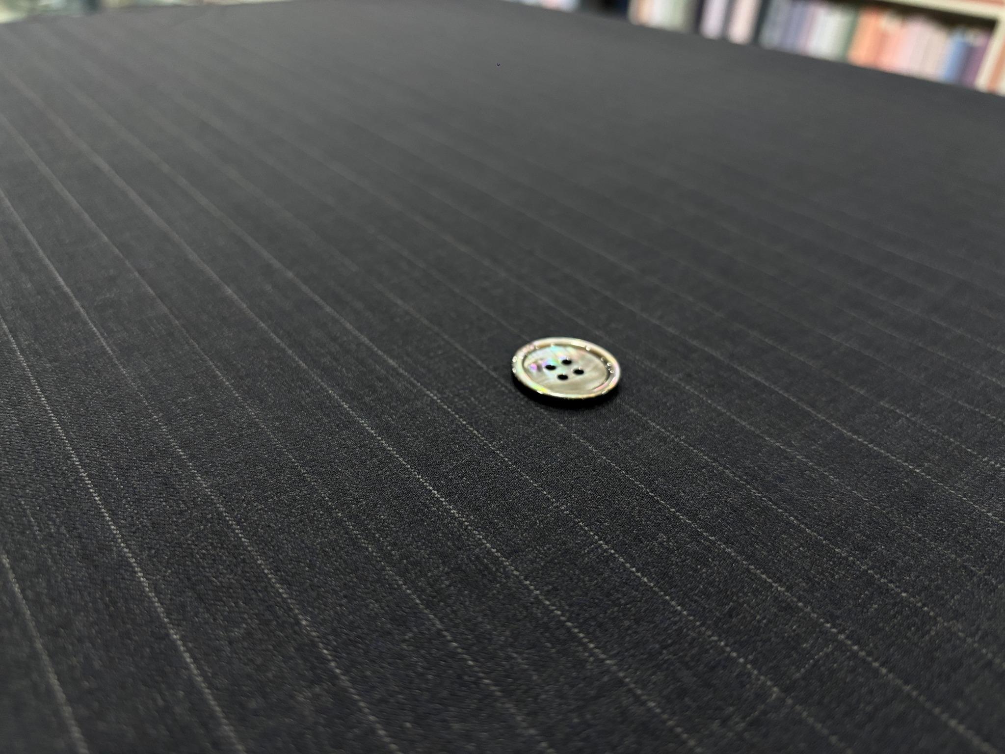 An iridescent grey four-hole button resting on charcoal pinstripe fabric.