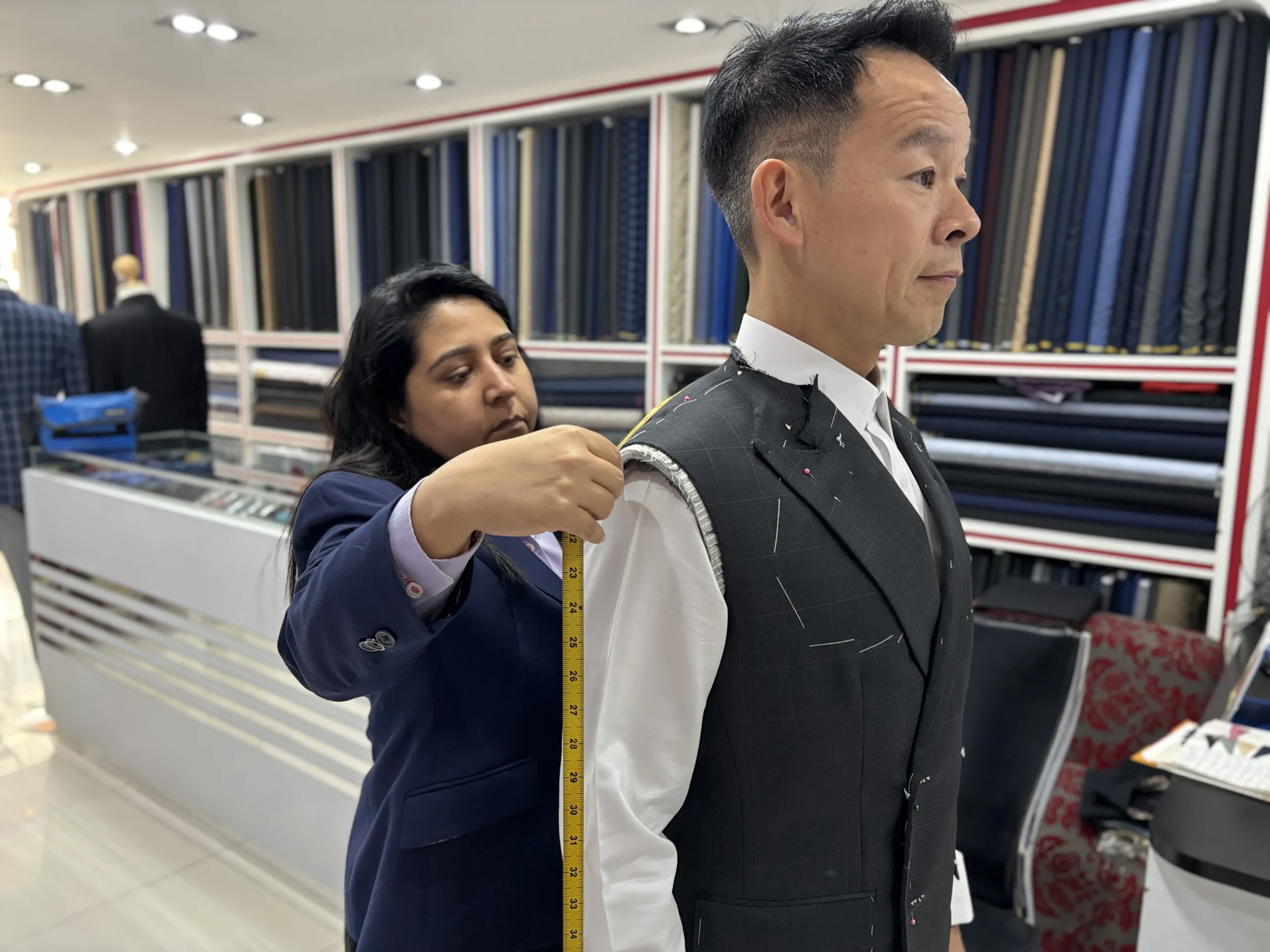 A fitter checks the shoulder area of an unfinished suit jacket on a client at Jhasper Fashion.